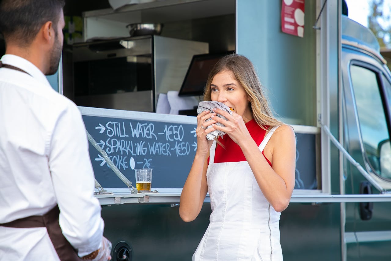 our-story-01 Calm woman in stylish clothes standing near food truck and eating tasty burger on street in daytime